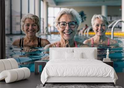 Three senior women with radiant smiles enjoying a healthy, active lifestyle during an aqua fitness session in an indoor swimming pool. Wall mural