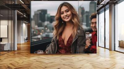 A cheerful young woman in a sequined red dress enjoys a social gathering with two male companions on a rooftop lounge. The city skyline looms in the soft focus background, twinkling with lights. Wall mural