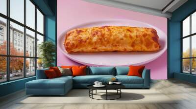 A golden brown pastry with a flaky crust and melted cheese on top, resting on a white plate against a pink background Wall mural