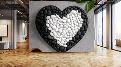 A heart-shaped arrangement of black and white stones on a textured surface, symbolizing love and harmony in decor. Wall mural