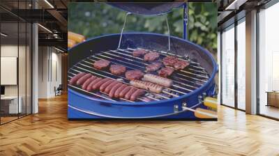 Close-up of a blue charcoal grill with sausages and meat patties cooking on the grate Wall mural