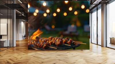 Close-up of sizzling meat skewers on a grill with flames, blurred background of a backyard party with string lights Wall mural