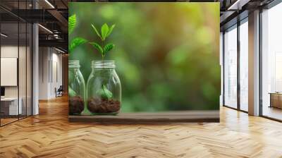 Two green seedlings growing in soil-filled glass jars with a blurred green background. Wall mural