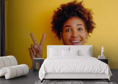 Portrait of beautiful young black woman in yellow top with short curly hair, smiling and making the peace sign on a yellow background, template for advertising or promotion, with copy space for text Wall mural