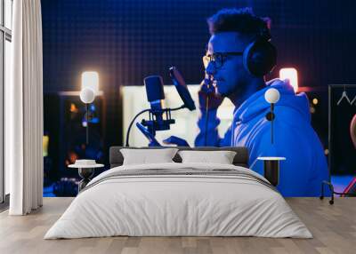 Male vocal artist, singer, podcaster with curly hair, headphones in sound studio recording new melody or album. Wall mural