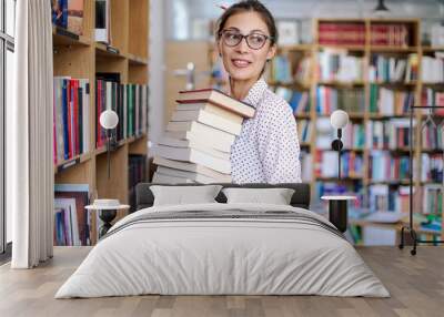 Young woman with a stack of books in library Wall mural