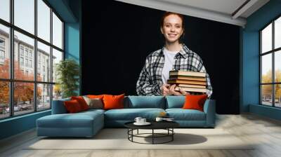 Cheerful young woman college student holding book and looking at camera on isolated black background. Pretty redhead lady model wearing casual fashion clothes emotionally showing facial expressions. Wall mural