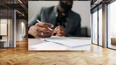 Close-up cropped shot of unrecognizable black businessman in suit sitting at office table and holding pen. Makes appointment notes time, writes important things and to-do list not to forget Wall mural