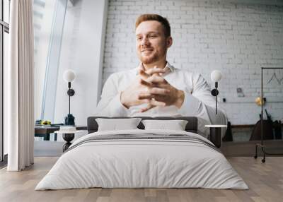 Close-up low-angle view of happy handsome young business man sitting at desk in modern office room and thinking looking away. Concept of successful worker, career advance and opportunity. Wall mural