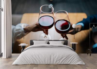 Close-up top view of unrecognizable loving man and woman clinking glasses with red wine sitting at table in restaurant. Cropped shot of couple enjoying nice romantic dinner, celebrating anniversary. Wall mural