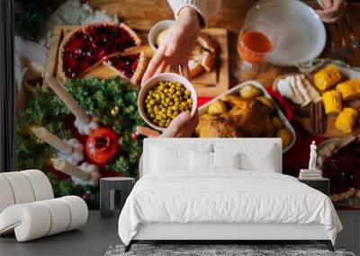 Close-up top view of unrecognizable young woman and man passing delicious food sitting at festive Christmas table during holiday family friendly party, selective focus. Wall mural