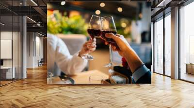 Close-up unrecognizable couple in love clinking glasses with red wine sitting at table in fancy restaurant at evening. Happy young man and woman enjoying nice romantic dinner, celebrating anniversary. Wall mural