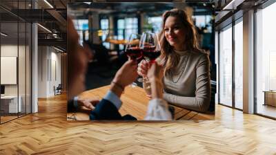 Close-up view from back of unrecognizable female clinking glass of red wine with cheerful friends sitting at table in fancy restaurant at evening. Happy three colleague enjoying dinner in cafe. Wall mural