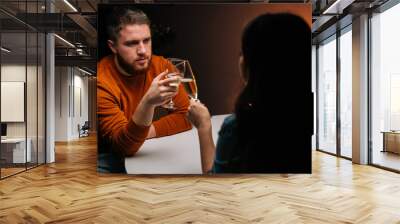 Closeup of serious young couple clinking glasses with champagne sitting at table with candles in cozy dark room. Loving man and woman celebrating anniversary, Valentines day, enjoying romantic date. Wall mural