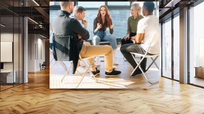 Diverse young colleagues sitting in circle have fun talking on business training with coach by window in light office room. Multiethnic business team discuss ideas engaged in educational meeting. Wall mural