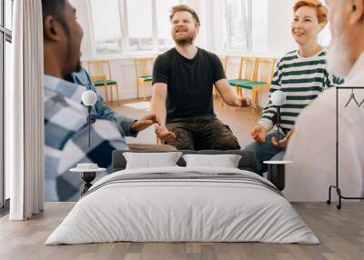 Group of happy multiracial people holding hands sitting in circle during therapy session. Cheerful multicultural and different ages men and women celebrating common progress and supporting each other. Wall mural