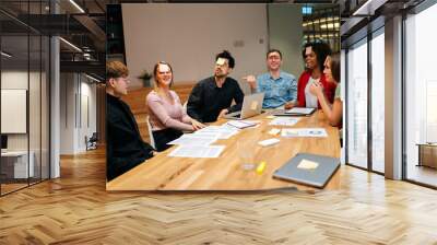 Multiethnic happy excited coworkers playing guessing game with sticky notes on forehead after work for entertainment. Cheerful diverse group of colleagues having fun together with charades in office. Wall mural