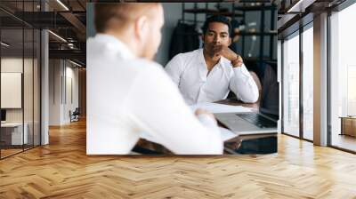 Pensive serious professional African American man interviewing caucasian European young candidate for job at successful company. Two business people talking strategy sitting at office desk. Wall mural