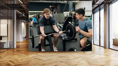 Portrait of male exercising support under supervision of personal coach. Trainer helping beginner sportsman for correct doing Scott Curls with barbell, lifting up EZ-bar sitting on preacher curl bench Wall mural