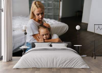 Portrait of tired cute little girl with closed eyes and loving caring mother comforting offended sad child daughter, showing love and care, expressing support, hugging, stroking hair sitting on floor. Wall mural