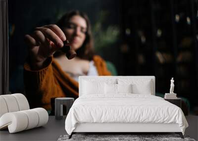 Selective focus of cute businesswoman in elegant eyeglasses making chess move sitting on armchair in dark room, on background of bookcase. Pretty intelligent lady playing logical game alone at home. Wall mural