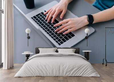 Top close-up view of hands of unrecognizable business woman typing on laptop keyboard sitting at desk with coffee cup in home office, selective focus. Wall mural