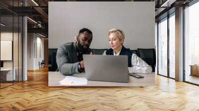 Two serious mixed-ages diverse business partners discussing online project, brainstorming on ideas at laptop, looking at display, talking, speaking, meeting at table in office, cooperating on tasks. Wall mural