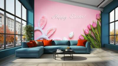 Top view of Easter eggs, pink tulips and two white fluffy bunny ears over pink background. Easter concept background. Happy Easter text. Wall mural