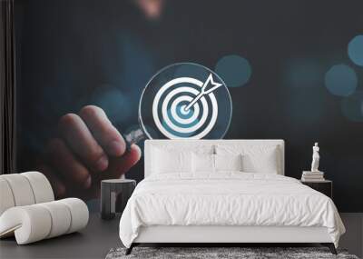 Businessman holding magnifier glass with white dartboard with arrow for setup and focus in objective target goal concept. Wall mural