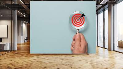 Hand holding magnify glass with red target board inside for focus and setup business objective target concept. Wall mural