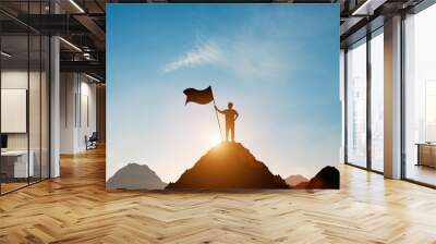 Silhouette of businessman holding flag on the top of mountain with over blue sky and sunlight. It is symbol of leadership successful achievement with goal and objective target. Wall mural