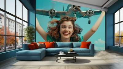 A smiling girl in a turquoise dress is flying a metal airplane with both hands, her eyes sparkling with joy. Wall mural