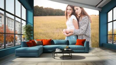 Two beautiful females are hugging on the grass field. Wall mural