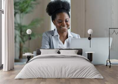 African businesswoman look on laptop screen with happy smile. Young ethnic office worker or boss female reading email on computer with successful good news, communicate with client online at workplace Wall mural