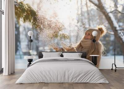 Attractive caucasian blonde woman with long hair throws snow up with a nice smile, bottom view. Happy young female plays with a snow in sunny winter day. Winter time concept Wall mural