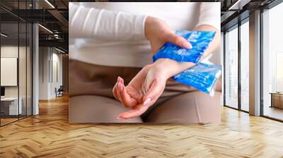 Close up of woman applying cold compress to a her painful wrist caused by prolonged work on the computer, laptop, selective focus on hand. Carpal tunnel syndrome, arthritis, neurological disease. Wall mural