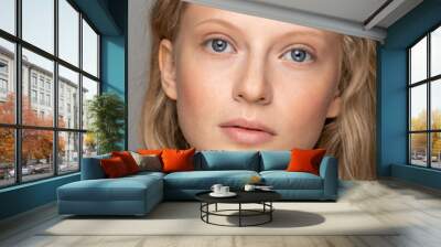 Close up of young woman face with blue eyes, curly natural blonde hair and eyebrows, has no makeup, looking at camera. Girl with perfect fresh clean skin over studio grey background. Youth concept.   Wall mural