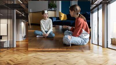 Guess who I am. Small children friends playing guessing game with sticky notes, brother and sister sitting on floor play together, two kids siblings enjoy spending time together during weekend at home Wall mural