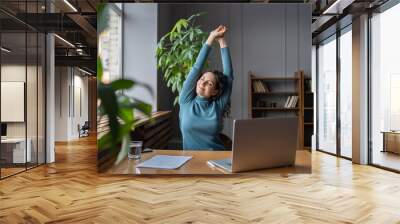 Happy businesswoman warming up body and muscles at workplace, feeling satisfied with work done, smiling female employee resting from computer screen. Well-being, productivity and happiness at work Wall mural