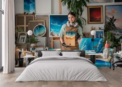 Happy craftswoman paints with epoxy resin, holding wooden kitchen board with seascape decoration, standing in art studio. Satisfied artist girl showing finished product made of liquid glossy material. Wall mural