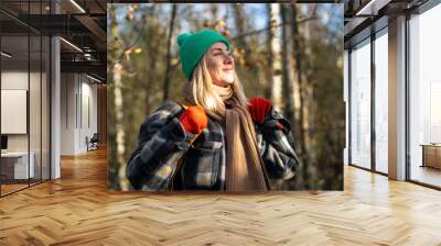 Joyful happy middle aged woman smiling looking aside walking in fall forest wearing warms clothes. Pleased female enjoys stroll, feels glad watching beauty of late autumn woods park in cold sunny day. Wall mural