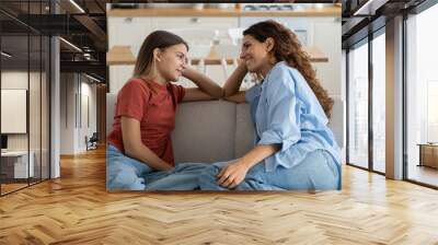 Loving mother listening to daughter with empathy and understanding while sitting together on sofa bonding at home, pre-teen girl child sharing secrets with mom, parent communicating with teenager Wall mural