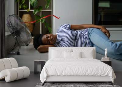 Overheated African woman lying on floor sleeping with electric fan on, enjoying fresh air, exhausted black female resting at home during extremely hot weather. Staying cool without air conditioning Wall mural