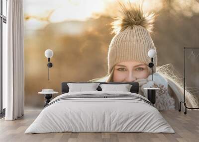 Portrait of young European woman with long hair in beige hat with fur pompon, scarf, coat, white gloves at sunny winter day/ Female wrap in and holding scarf, smiling, looking at camera, copy space Wall mural