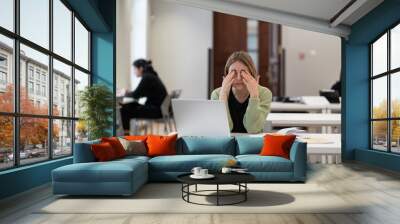 Sleepy adult female student rubbing eyes, feeling tired after studying for long hours in library, exhausted middle-aged woman feeling feel no motivation to study while getting new qualification Wall mural