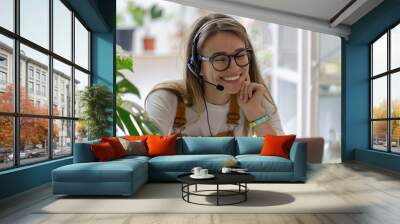 Smiling gardener millennial woman wear headphones talk video calling, using laptop, communicating with clients, watching webinar or video stream conference, remote work from home. Distance education. Wall mural