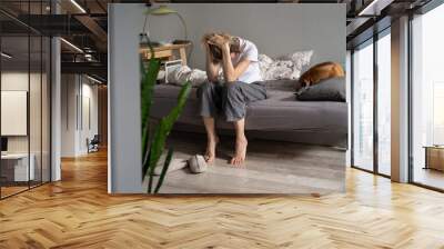 Unhappy woman sitting on sofa holding head in hands suffering from hangover headache in morning, female having personal problems. Living alone and depression, mental health problems in midlife Wall mural