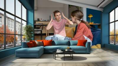 Young angry emotional mother screaming at troubled teen daughter, furious parent mom dealing with teenage behavior problems, yelling at upset adolescent girl while sitting together on sofa at home Wall mural