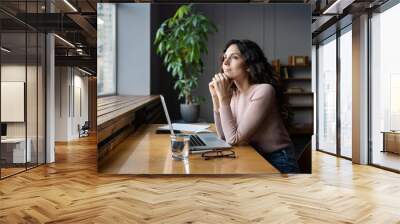 Young dreamy smiling female entrepreneur thinking about business goals and objectives, enjoying good window view while working in office, pleased businesswoman resting from computer work Wall mural