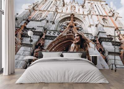 A romantic walk of the bride and groom through the city streets. Newlyweds on the background of the cathedral. Wall mural